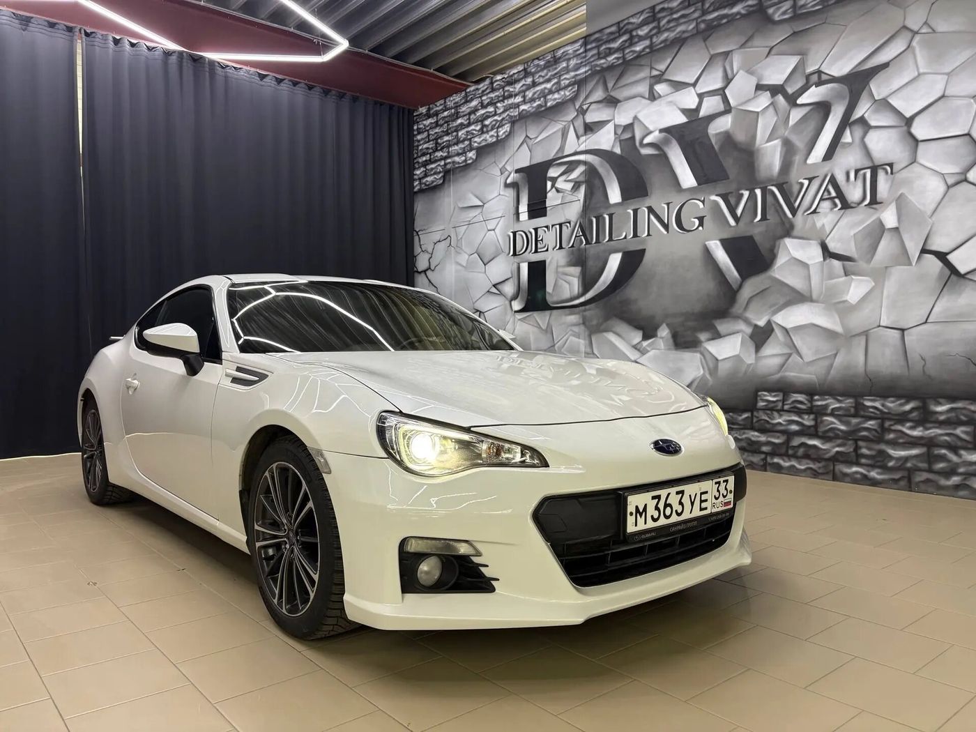 Белый Subaru на фоне стены с надписью Detailing Vivat
