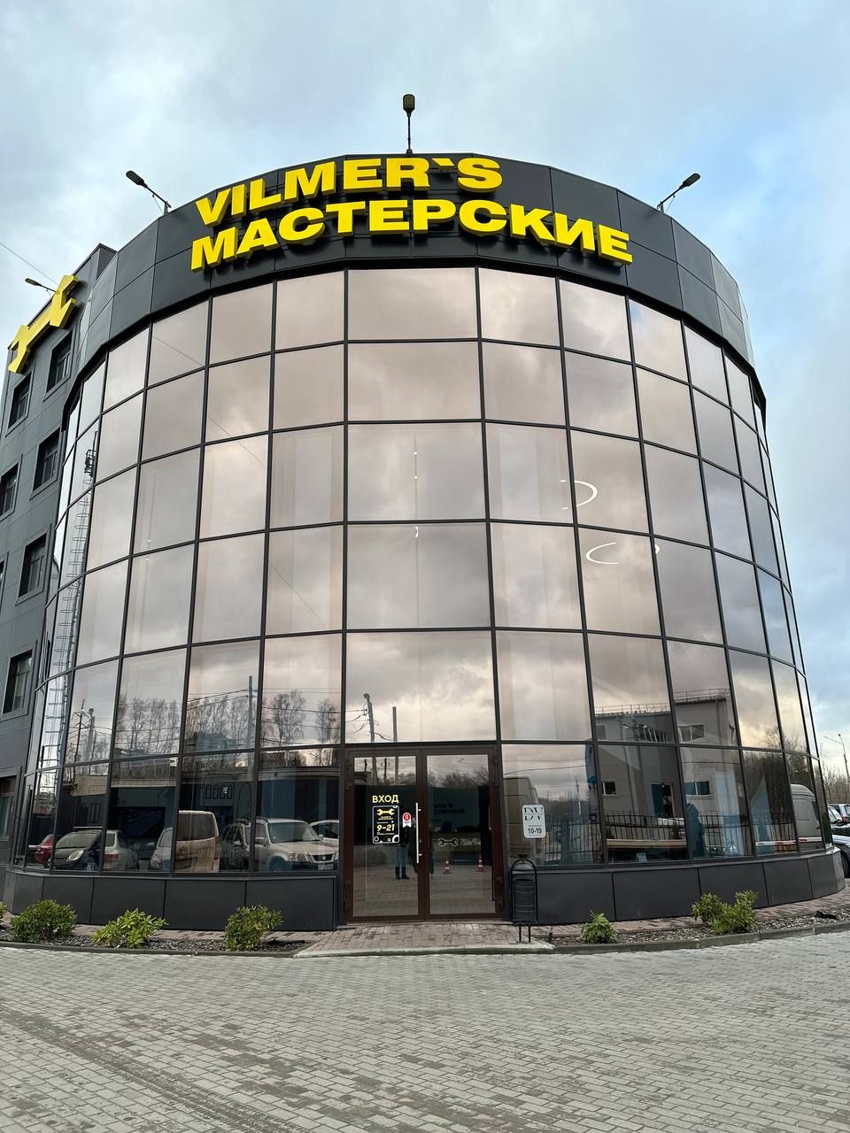 Круглое стеклянное здание с вывеской Vilmer's Мастерские и входом