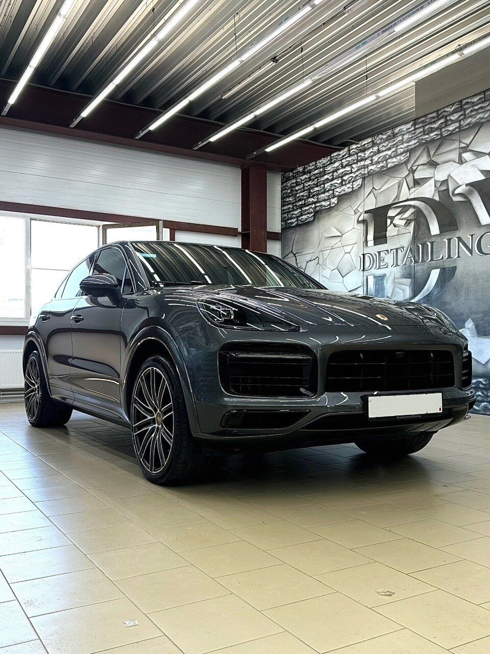 Серый Porsche Cayenne на фоне стены с логотипом Detailing Vivat