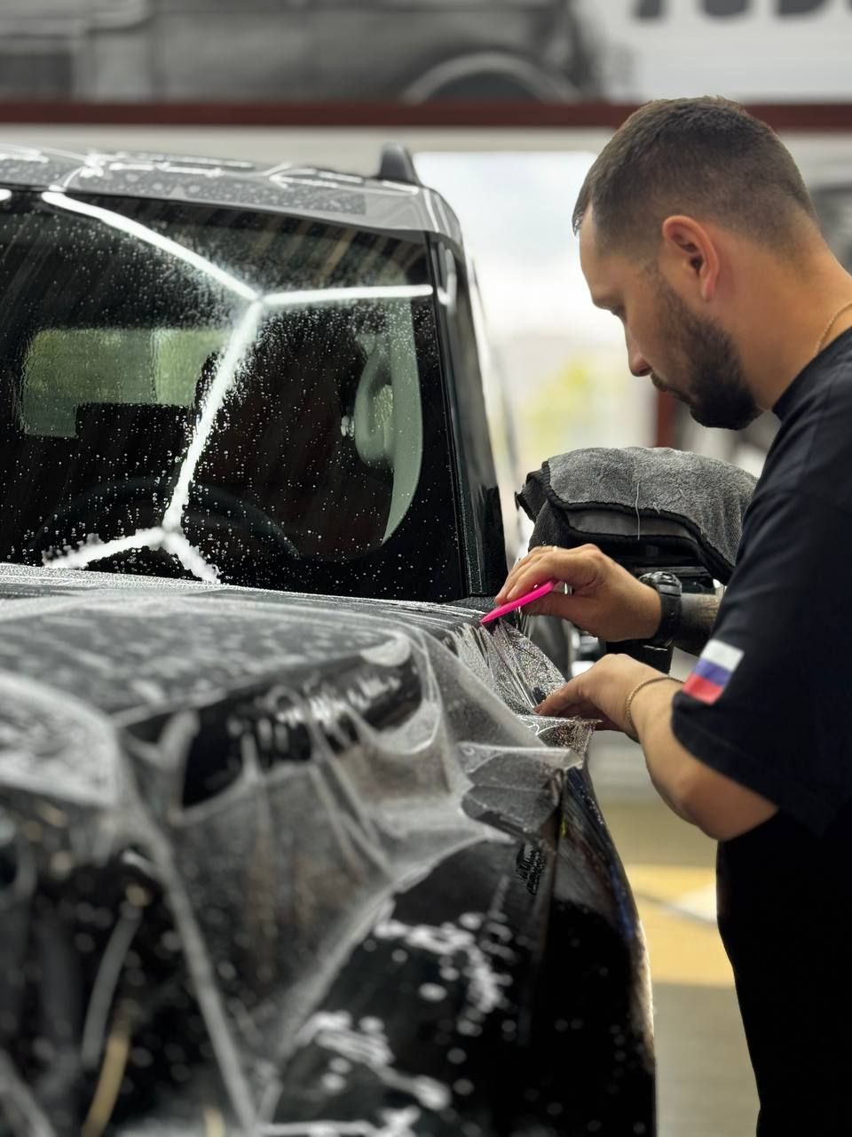 Мастер разглаживает плёнку на кузове автомобиля