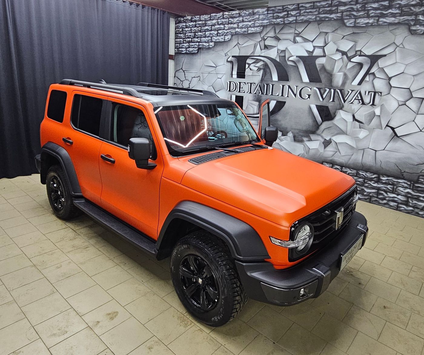 Оранжевый внедорожник в студии на фоне стены с надписью Detailing Vivat